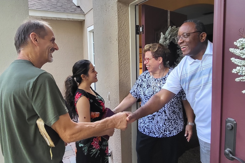 Two people with Bibles being welcomed into a home